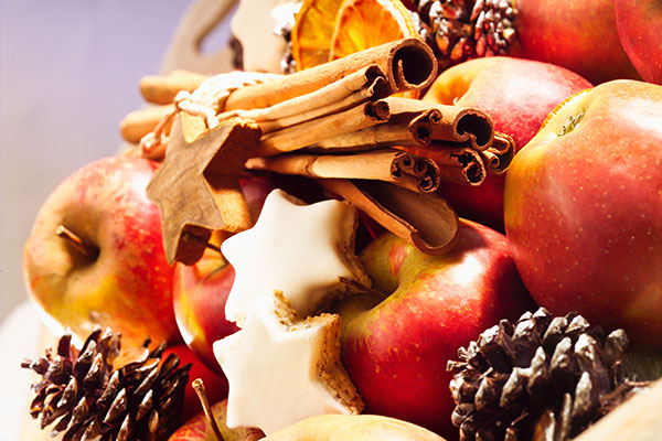 Arrangement aus weihnachtlichen Zutaten (Zimtsterne, Zimtstange, Äpfel, Tannenzapfen und Orangenscheiben).